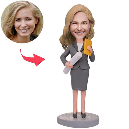 Vrouwelijke ingenieur met blauwdrukken en gepersonaliseerde bobblehead, gemaakt door MadeMine, met gegraveerde tekst op de afbeelding.